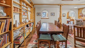A dining room with a wooden table and chairs, surrounded by bookshelves filled with books and decorative items. - Encanto Lodge - Downtown Chama 1 Block From Train (Chama)