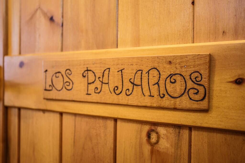 Une enseigne en bois portant l’inscription « LOS PAJAROS », fixée à un mur en bois.