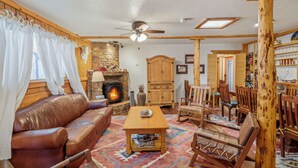 A cozy living room with a leather sofa, wooden coffee table, and a fireplace. - Encanto Lodge - Downtown Chama 1 Block From Train (Chama)