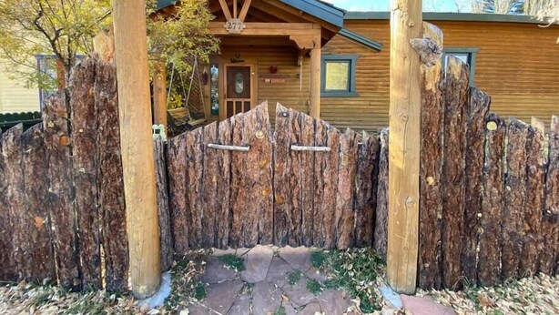 A wooden cabin with a rustic design, a stone pathway leading to the entrance, and a wooden fence with a unique texture. - Encanto Lodge - Downtown Chama 1 Block From Train (Chama)