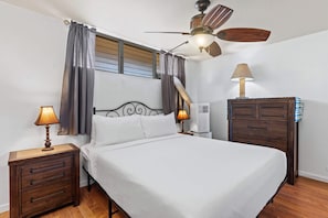Quarto com uma cama, duas mesas de cabeceira, um criado-mudo, ventilador de teto, ar condicionado e cômoda.