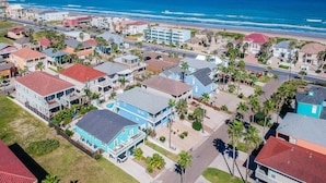 Vue aérienne d’une zone résidentielle côtière, avec des maisons, une plage et un ciel bleu dégagé.