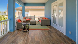 Un espace extérieur abrité, aménagé avec des meubles en osier, un tapis à rayures et offrant une vue sur un bâtiment en arrière-plan.