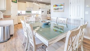 Une cuisine moderne avec des meubles blancs, une table à manger en verre et des chaises blanches.