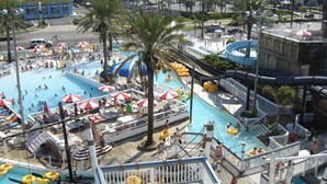 A large outdoor swimming pool with multiple lanes, surrounded by palm trees and umbrellas.