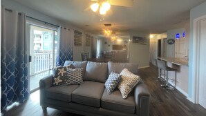 A living room with a gray sofa, patterned cushions, a ceiling fan, and a view of the dining area.