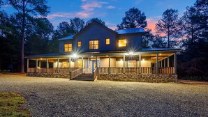 A two-story house with a stone foundation, a porch with railings, and multiple windows. - THE PORCH AT BROKEN BOW 5b/6ba/Sleeps 20 - 2pm Checkout! Loads of amenities! (Broken Bow)