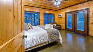 A wooden cabin bedroom with a bed, a chair, and a window. - THE PORCH AT BROKEN BOW 5b/6ba/Sleeps 20 - 2pm Checkout! Loads of amenities! (Broken Bow)