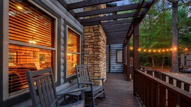 A wooden deck with outdoor seating and a stone wall. - THE PORCH AT BROKEN BOW 5b/6ba/Sleeps 20 - 2pm Checkout! Loads of amenities! (Broken Bow)