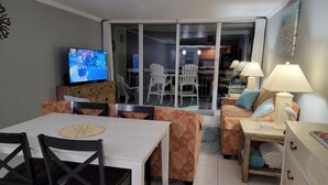 Un salon comprenant un téléviseur, une table à manger, des chaises, un canapé et des lampes.