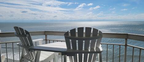 A balcony with Adirondack chairs and a table overlooking the ocean.