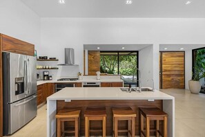 A modern kitchen with a central island, bar stools, and a large window.