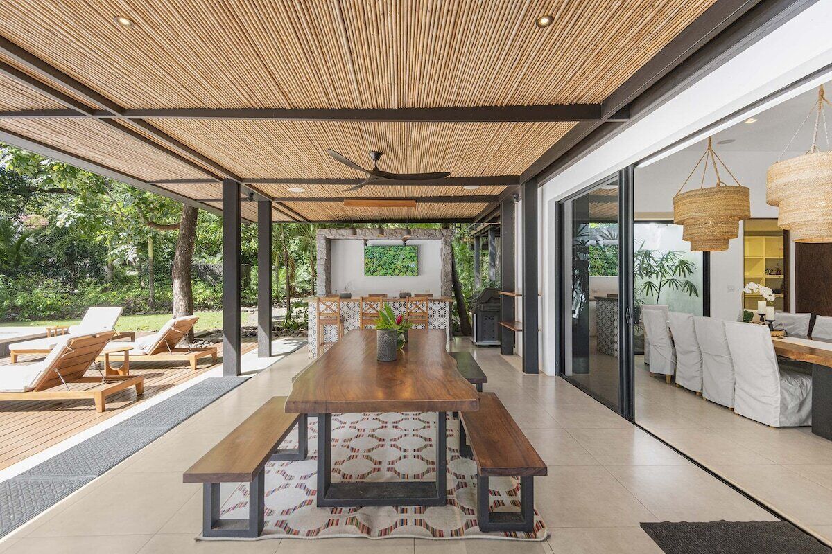 An open-plan living area with a wooden dining table, benches, and a view of the outdoors.