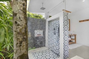 Ein modernes Badezimmer mit einer Steinwand, einer Dusche mit geometrischem Fliesendesign und einer Holzablage.