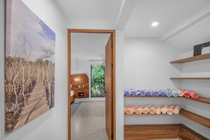A hallway with a wooden door leading to a bedroom, a wooden shelf with towels, and a large landscape painting on the wall.