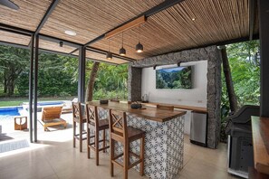 An outdoor kitchen with a stone wall, bar stools, and a TV.