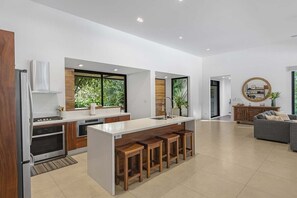 A modern kitchen with a central island, wooden bar stools, and a dining area with a sofa.