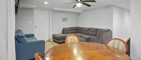 Ein Wohnzimmer mit grauem Ecksofa, einem blauen Sofa und einem Holzesstisch mit Stühlen.