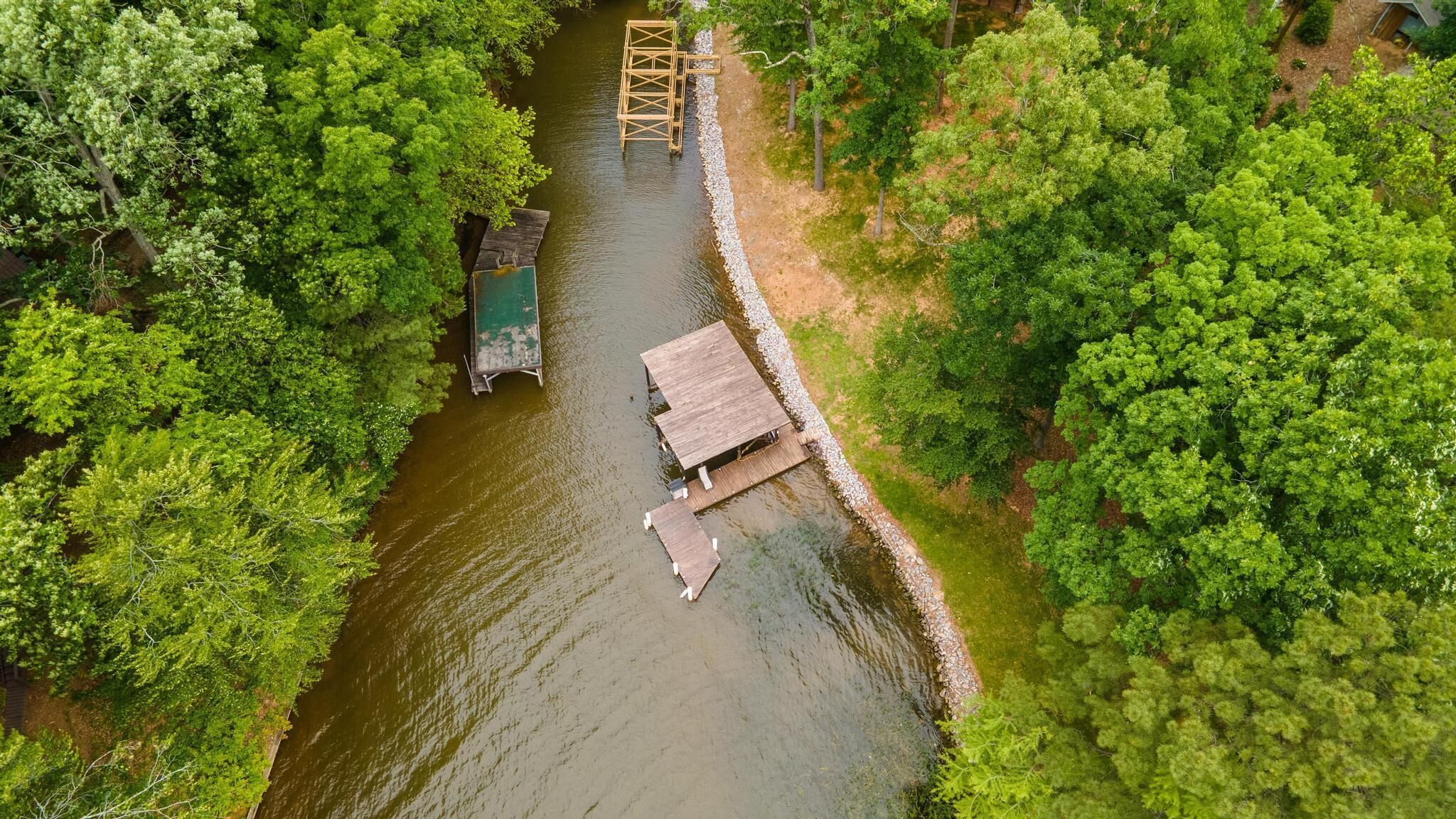 Vue aérienne d’un quai en bois au bord de la rivière, avec un petit bâtiment, le tout entouré d’une végétation luxuriante.