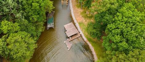 Vue aérienne d’un quai en bois au bord de la rivière, avec un petit bâtiment, le tout entouré d’une végétation luxuriante.