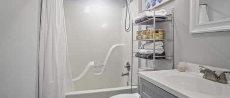 Un baño con bañera, inodoro y estante con toallas y artículos de aseo.