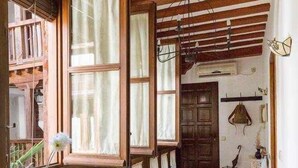 Un comedor con mesa y sillas de madera, ventanas amplias con cortinas y piso de baldosas.