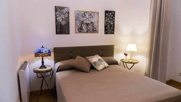 Une chambre à coucher avec un lit, deux tables de chevet avec des lampes, un radiateur et trois œuvres d’art encadrées accrochées au mur.