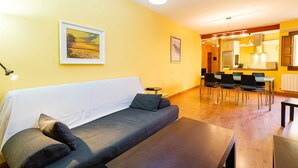 A living room with a sofa, a dining table, and chairs. There is a kitchen area visible through an open doorway. - Apartamento San Vicente by Toledo AP (Toledo)
