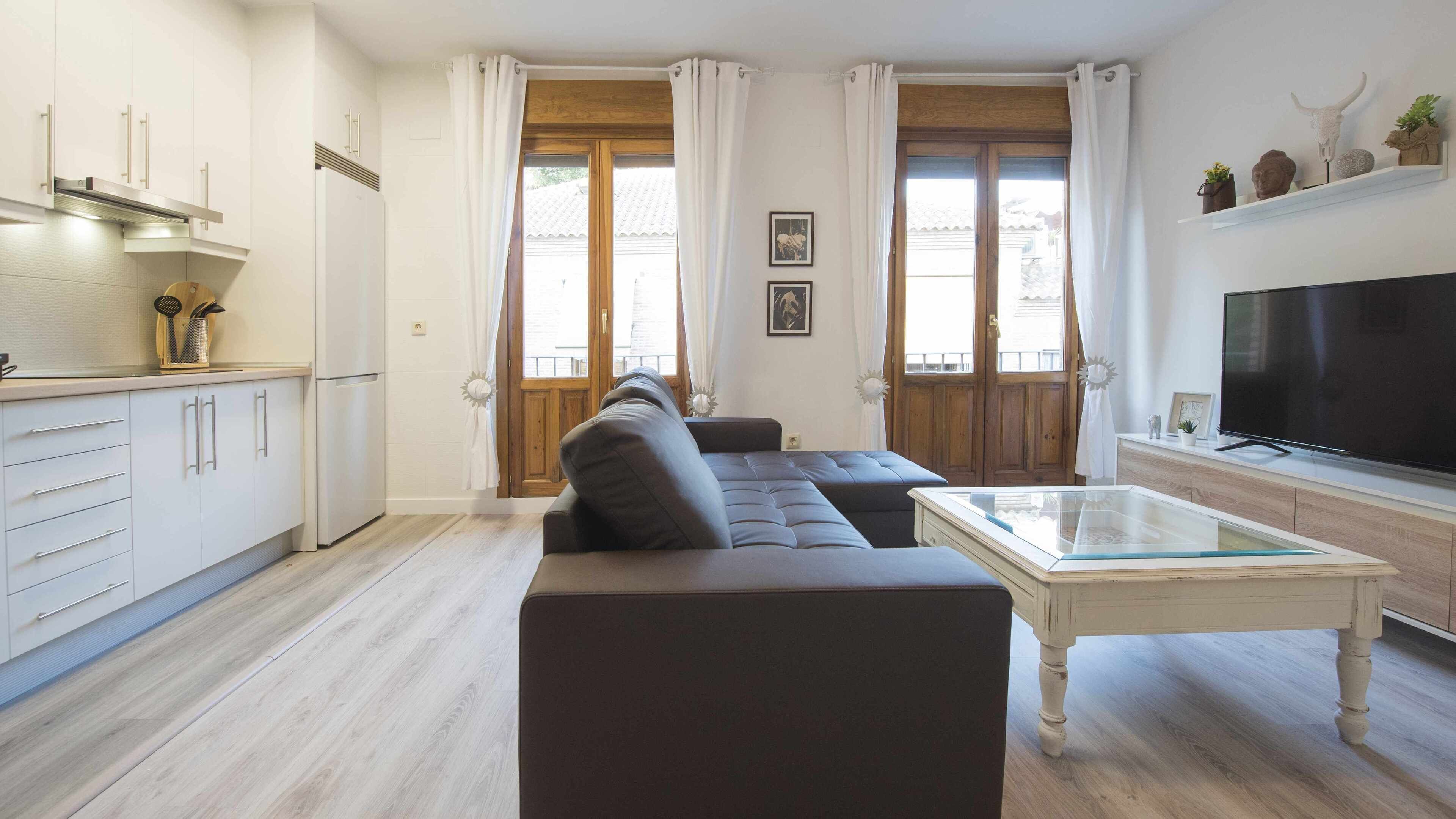 Ein modernes Wohnzimmer mit einer Couch, einem Fernseher und einer Küchenzeile inklusive Schränke und Kühlschrank.
