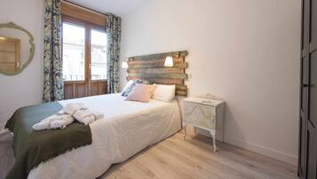 Un dormitorio con cama, mesita de noche, cabecera de madera y ventana con cortinas.