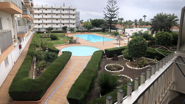 Un edificio residencial con piscina, jardines bien cuidados y vistas a palmeras circundantes.