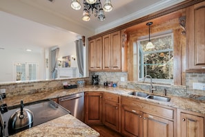 A kitchen with granite countertops, wooden cabinets, a stainless steel sink, and a window with a view of trees.