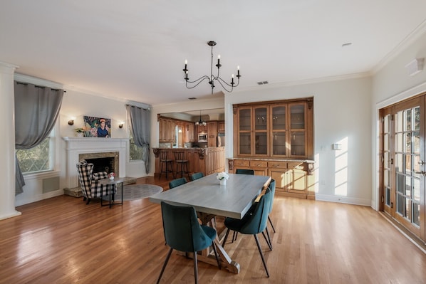 A spacious dining area with a large table and chairs, a fireplace, and a kitchen in the background.