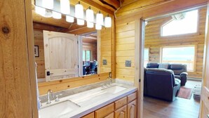 Ein Interieur einer Holzhütte mit einem Waschbecken-Doppelplatz, einem großen Spiegel und einer Sitzecke mit Sofa und Sesseln.