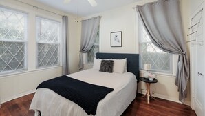 A bedroom with a bed, a ceiling fan, a nightstand, and a window with curtains.