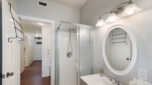 A bathroom with a walk-in shower, a large mirror, and a white sink.