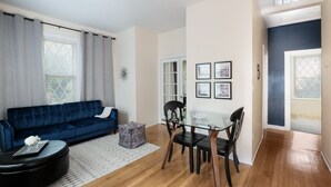 Una sala de estar con un sofá azul, una mesa de comedor de vidrio y un otomano negro.