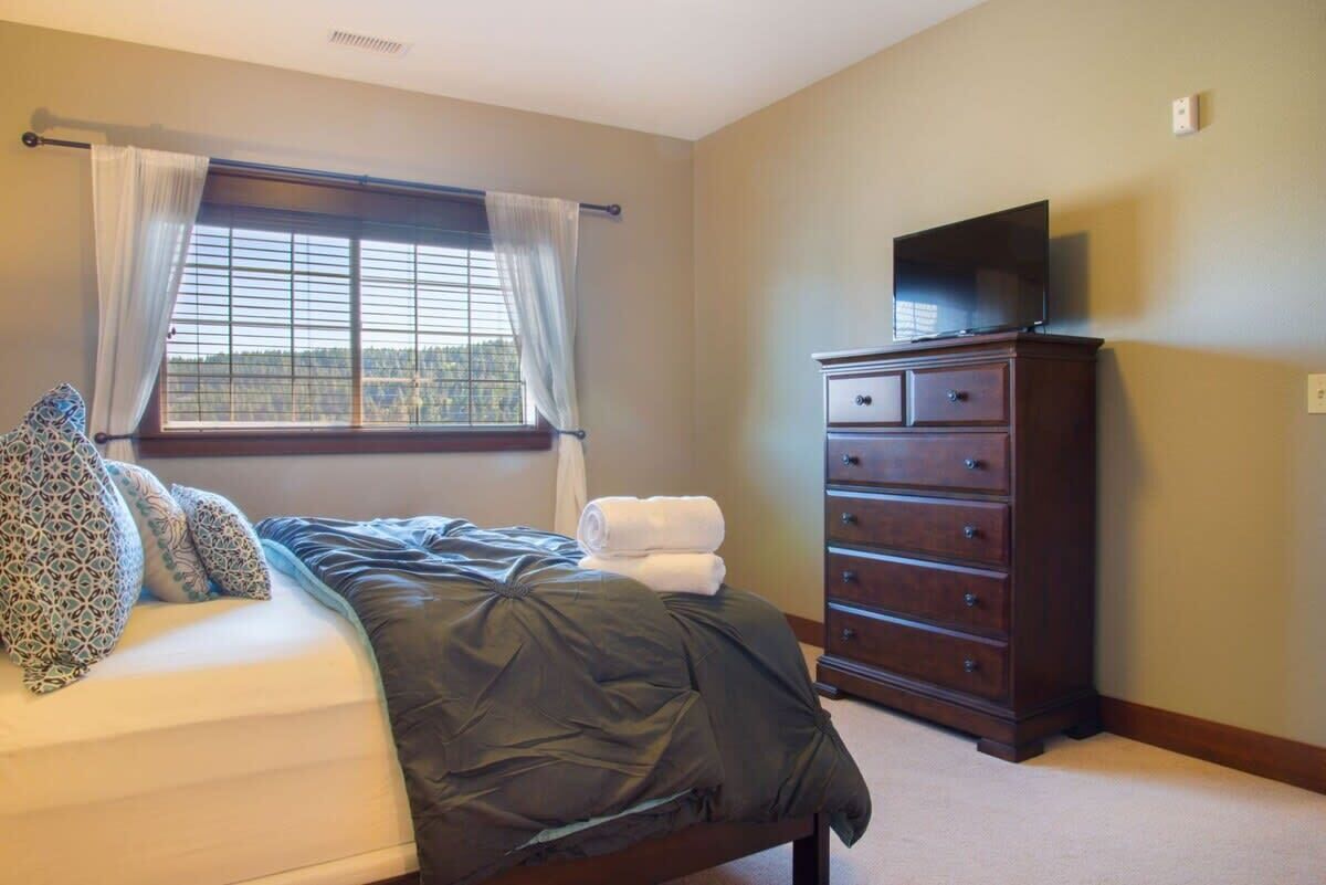 A bedroom with a bed, a dresser, a television on top of the dresser, and a window with curtains.