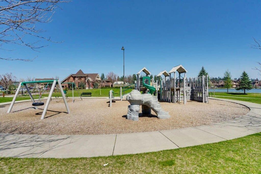 A playground with swings, climbing structures, and a large rock sculpture.