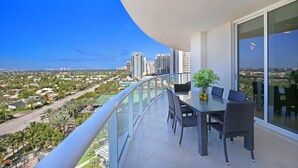 A balcony with a dining table and chairs, overlooking a cityscape with tall buildings and palm trees. - Luxury Condo in the Ritz Carlton Residences on a private beach  (Riviera Beach)