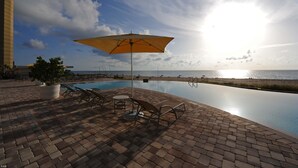 A poolside area with lounge chairs and an umbrella, overlooking a beach and ocean. - Luxury Condo in the Ritz Carlton Residences on a private beach  (Riviera Beach)