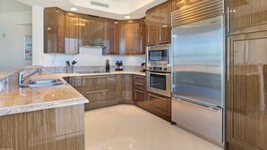 A modern kitchen with wooden cabinets, stainless steel appliances, and a granite countertop. - Luxury Condo in the Ritz Carlton Residences on a private beach  (Riviera Beach)