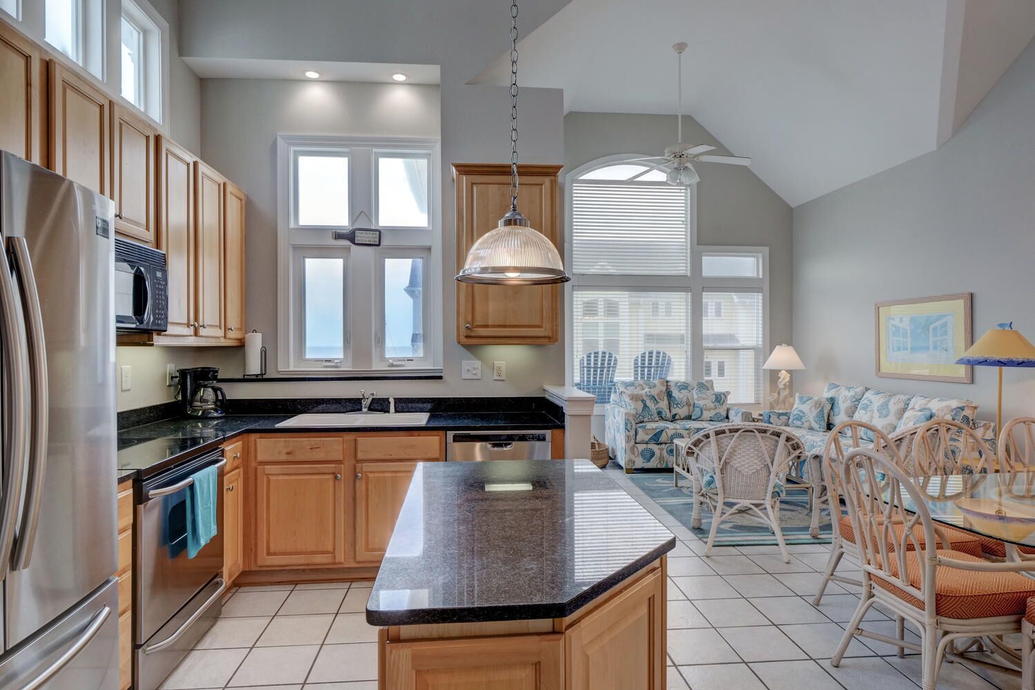 A modern kitchen with wooden cabinets, a granite countertop, and a dining area with wicker furniture.