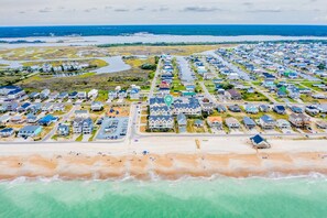 Vue aérienne d’une zone résidentielle côtière, avec des maisons, une plage et un port de plaisance.