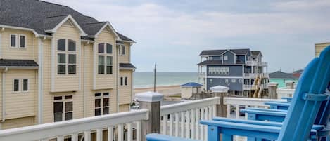 A beachfront property with a wooden deck and blue chairs, overlooking the ocean and beach.