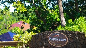 A sign for Poipu Crater with a stone wall and lush greenery in the background.