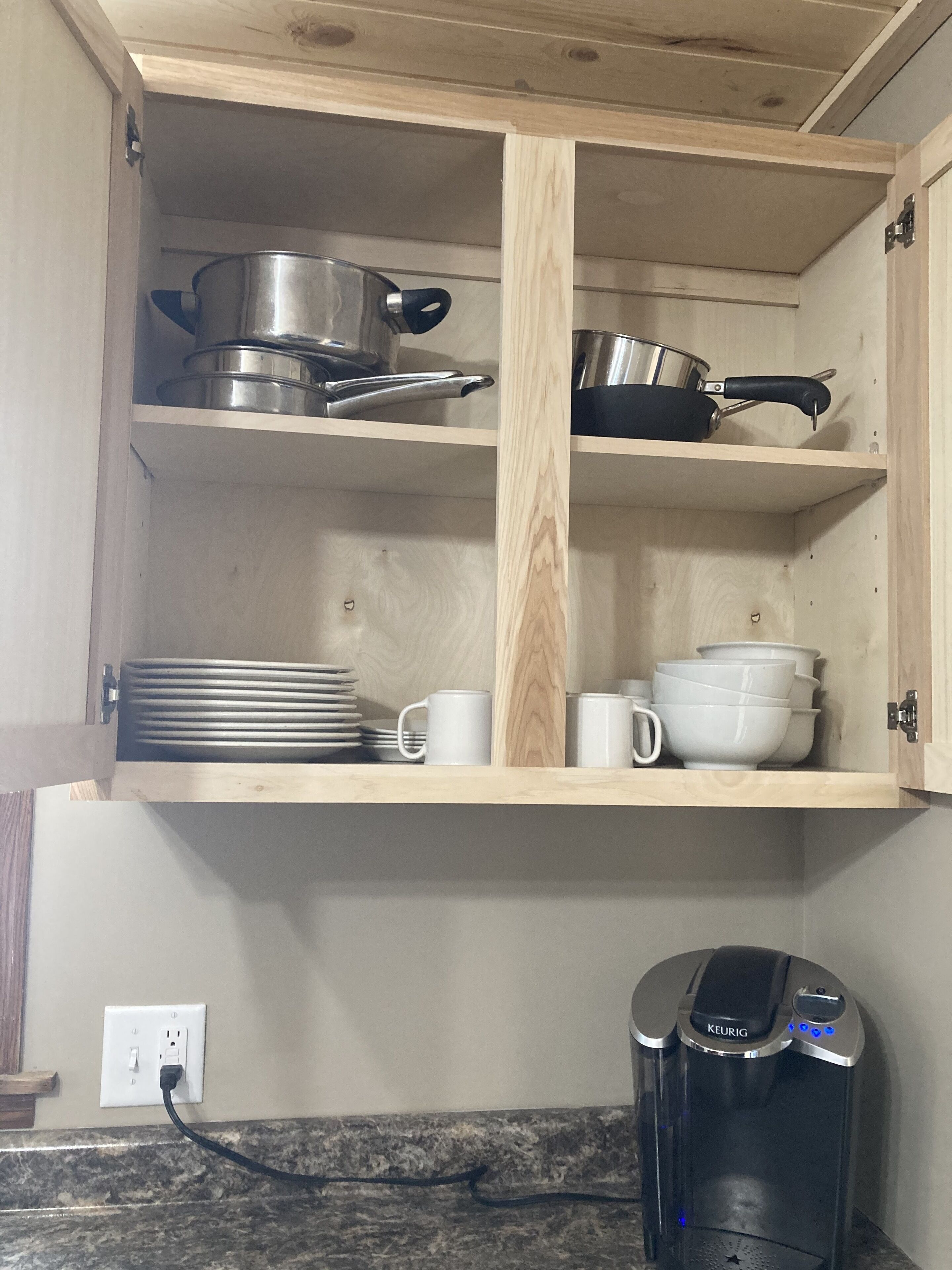A kitchen with wooden shelves holding cookware, plates, and mugs. A coffee maker is on the counter.