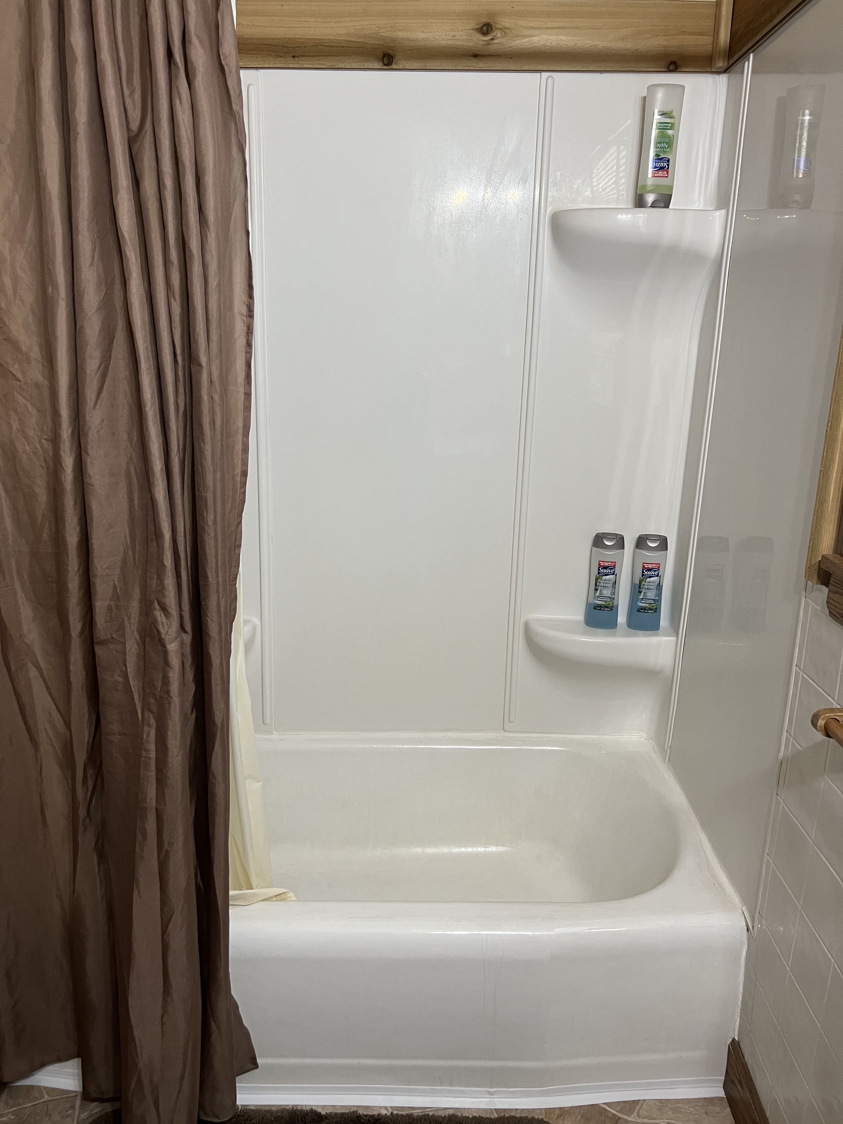 Un baño con bañera, cortina de ducha y estante con artículos de aseo.