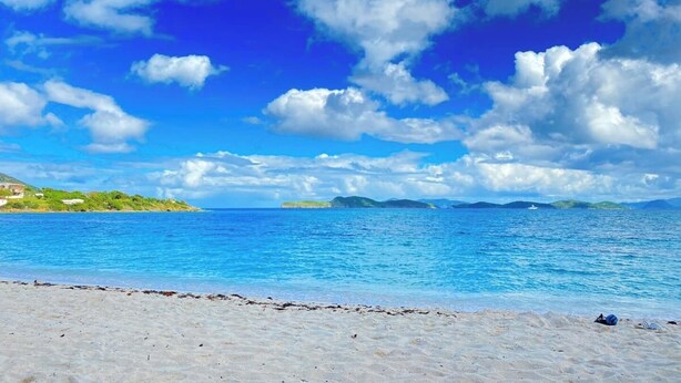 Une plage avec une eau d’un bleu limpide et un rivage sablonneux.