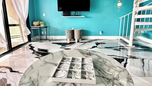 Un salon moderne avec un mur de couleur turquoise, un téléviseur à écran plat fixé au-dessus d’une table basse en marbre et un escalier en colimaçon blanc.